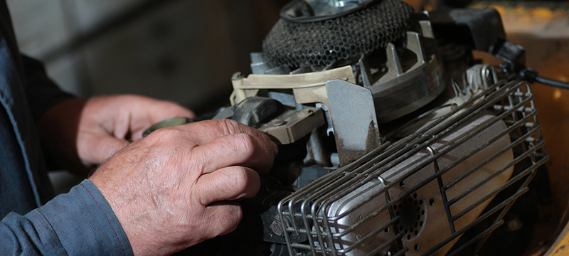 A man works on a lawnmower engine.