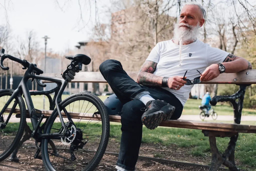 Male Model sitzt mit angelehntem Fahrrad auf Bank, tex–lock eyelet um Sattelstange gewickelt